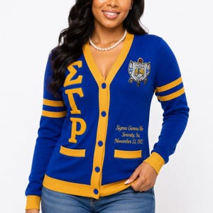 May include: A royal blue V-neck cardigan with gold trim, featuring the Greek letters SGRho on the right side, a crest on the left chest, and the text Sigma Gamma Rho Sorority, Inc. November 12, 1922 embroidered in gold on the lower left front.