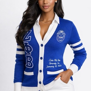 May include: A blue cardigan sweater with white accents, featuring the letters "Zeta" on the front and the sorority's crest. The sweater has white stripes on the sleeves and the text "Zeta Phi Beta Sorority, Inc. January 16, 1920".
