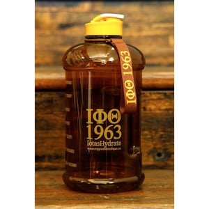 May include: A brown plastic water bottle with a yellow lid and a brown strap. The bottle has a gold logo that says "IΦΘ 1963 lotasHydrate www.mygreekboutique.co".
