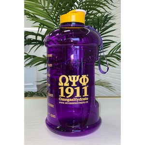 May include: Purple water bottle with a yellow lid and a gold Omega Psi Phi 1911 logo. The bottle has a carrying strap and a motivational quote on the side.
