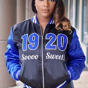 May include: Black and blue satin bomber jacket with white trim and the numbers "19 20" in blue. The text "Soooo Sweet!" is embroidered below the numbers. The jacket has a zipper closure and blue sleeves.