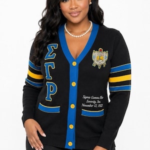 May include: A black V-neck cardigan featuring blue trim and yellow buttons. The right side displays vertical Greek letters, while the left side features a crest and the text Sigma Gamma Rho Sorority, Inc. November 12, 1922. Sleeves have blue and yellow stripes.