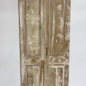 May include: A pair of antique wooden doors with a distressed white paint finish. The doors have four raised panels each and are made of solid wood.