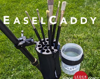 May include: A black easel caddy with a brush holder and a container for water or other liquids. The caddy is attached to a black easel pole. The text "Easel Caddy" is visible at the top of the image. The text "www.ledereasel.com" is visible at the bottom of the image.