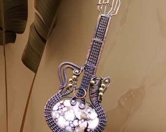 May include: A wire-wrapped guitar sculpture with a white and brown stone inlay. The guitar is made of copper wire and has a gold-colored finish. The stone inlay is set in the body of the guitar and has a natural, organic pattern.