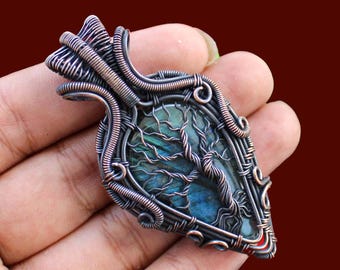 May include: A handcrafted pendant with a leaf-like shape, featuring a blue-green stone encased in intricate copper wire. The wirework forms a tree design within the stone, creating a unique and artistic piece of jewelry.