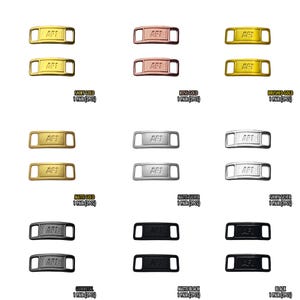 May include: A collection of shoe lace tags in various metallic finishes, including shiny gold, rose gold, brushed gold, matte gold, matte silver, shiny silver, gunmetal, matte black, and black. Each tag has the letters "AFT" engraved.