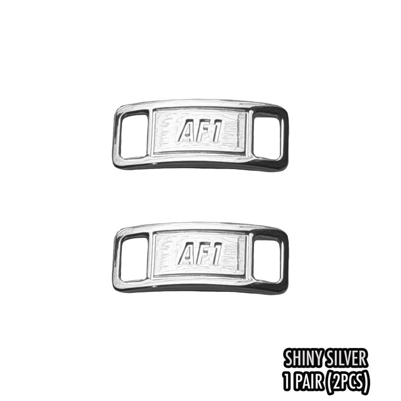 May include: Two shiny silver AF1 shoelace tags. Each tag is rectangular with rounded edges and features the letters "AF1" in the center. The tags have a polished, reflective surface. The text "SHINY SILVER 1 PAIR (2PCS)" is at the bottom.