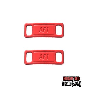 May include: Two bright red rectangular shoe accessories with the text "AF1" embossed on each. Each accessory has two holes. The text "BRIGHT RED 1 PAIR (2PCS)" is in the bottom right corner.