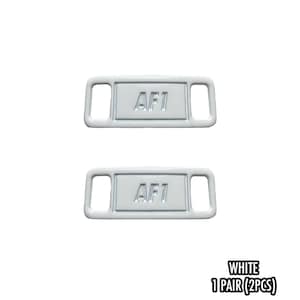 May include: Two white shoe lace tags with the text "AF1" in the center. The tags have a rectangular shape with rounded corners and two rectangular holes on each side. The text "WHITE 1 PAIR (2PCS)" is at the bottom.