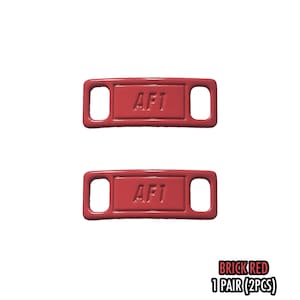 May include: Two brick red shoe tags with the text "AF1" embossed on each. The tags have a rectangular shape with rounded corners and two holes for laces. The bottom right corner of the image has the text "BRICK RED 1 PAIR (2PCS)".
