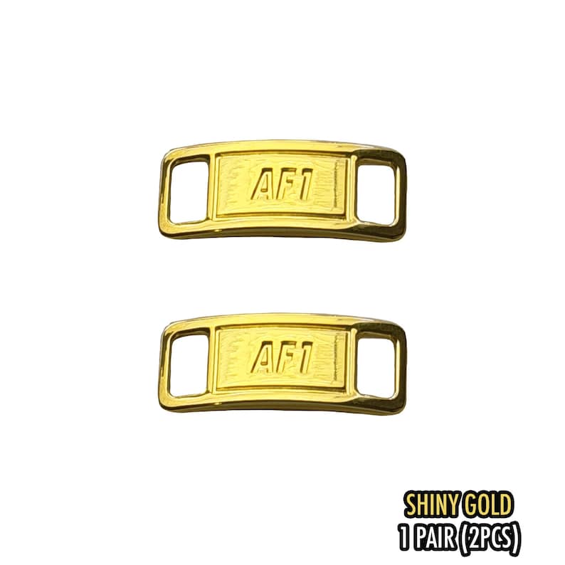 May include: Two shiny gold AF1 shoe lace tags. Each tag is rectangular with rounded corners and a rectangular opening on each end. The text "AF1" is embossed on the front. The text "SHINY GOLD 1 PAIR (2PCS)" is in the bottom right corner.