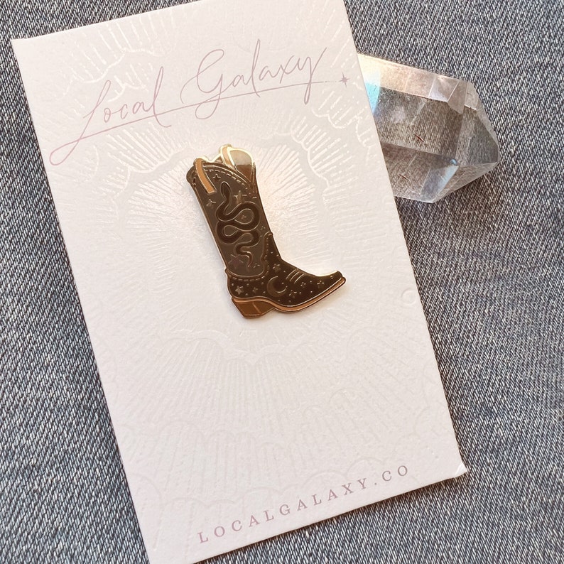 Op de afbeelding: Gouden emaille pin met een bruine cowboylaars met een slang- en sterrenontwerp. De pin is op een witte kaart met de tekst "Local Galaxy" en "LocalGalaxy.co".