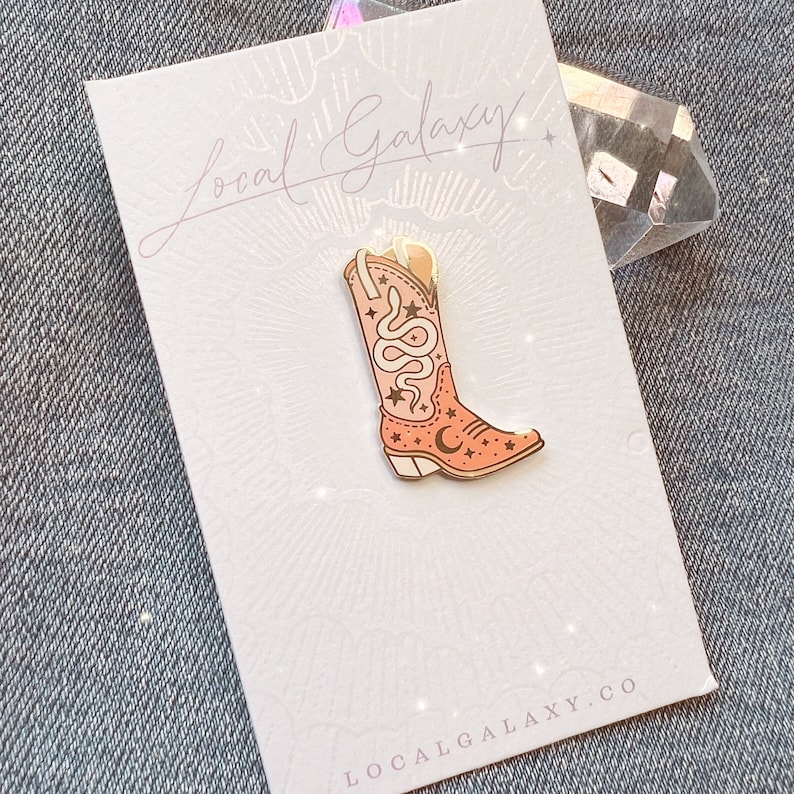 Op de afbeelding: Een roze emaille pin met een cowboylaars met een slang- en sterrenontwerp. De pin is op een witte kaart met de tekst "Local Galaxy" en "localgalaxy.co".