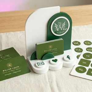 May include: A white and dark green acrylic business card display stand featuring a circular logo with the text Willow Layer. The set includes a stack of rectangular green business cards and a sheet of circular stickers with the same logo.