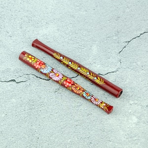 Könnte beinhalten: Zwei Holzstäbchen mit roter Farbe und Blumendesigns. Die Stäbchen sind mit bunten Blumen und Blättern bemalt.