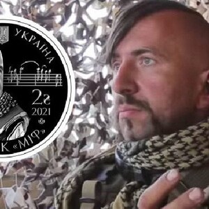 May include: A black and white commemorative coin featuring a portrait of a man with a mustache and a traditional Ukrainian headdress. The coin has the text "Василь Сліпак" and "2021" inscribed on it.