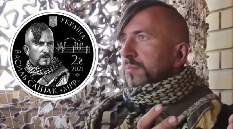 May include: A black and white commemorative coin featuring a portrait of a man with a mustache and a traditional Ukrainian headdress. The coin has the text "Василь Сліпак" and "2021" inscribed on it.