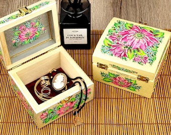 May include: Wooden jewelry boxes with floral designs. One box is open, revealing jewelry inside. The boxes are painted with pink and green flowers. The text "COCKTAIL IN KHARKIV" is on a black bottle in the background.