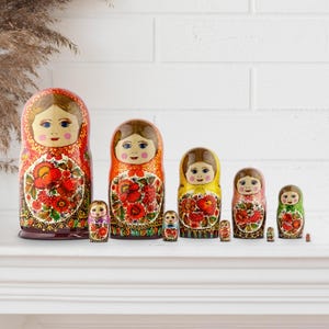 Puede incluir: Un conjunto de mu&ntilde;ecas rusas tradicionales, o mu&ntilde;ecas Matrioska, de varios tama&ntilde;os. Las mu&ntilde;ecas presentan caras pintadas y dise&ntilde;os florales en rojo, naranja, amarillo y verde. La mu&ntilde;eca m&aacute;s grande mide unos 18 cm de altura.