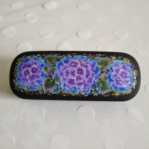 May include: Black rectangular glasses case with a hand-painted design of purple and blue flowers. The flowers are arranged in a row across the case.