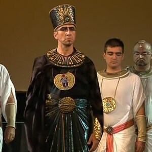 May include: A group of men wearing elaborate costumes, including a pharaoh with a tall headdress and a gold-colored collar. The men are standing in a line, and they are all looking at the camera.