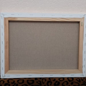 May include: The back of a stretched canvas painting with a wooden frame. The canvas is white and the frame is a light brown color.