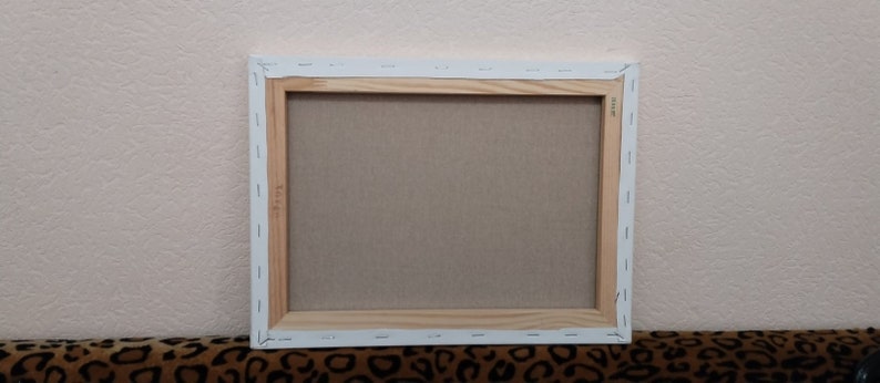 May include: The back of a stretched canvas painting with a wooden frame. The canvas is white and the frame is a light brown color.