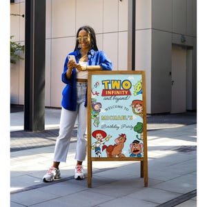 May include: Wooden A-frame sign with a light blue background featuring characters from the movie Toy Story. The sign reads "TWO INFINITY and beyond!" and "Welcome to Michael's Birthday Party".