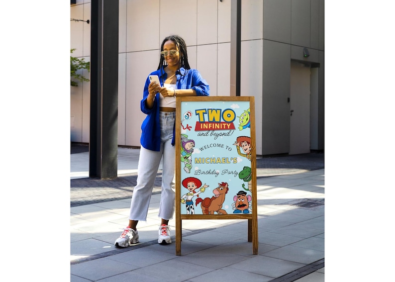 May include: Wooden A-frame sign with a light blue background featuring characters from the movie Toy Story. The sign reads "TWO INFINITY and beyond!" and "Welcome to Michael's Birthday Party".