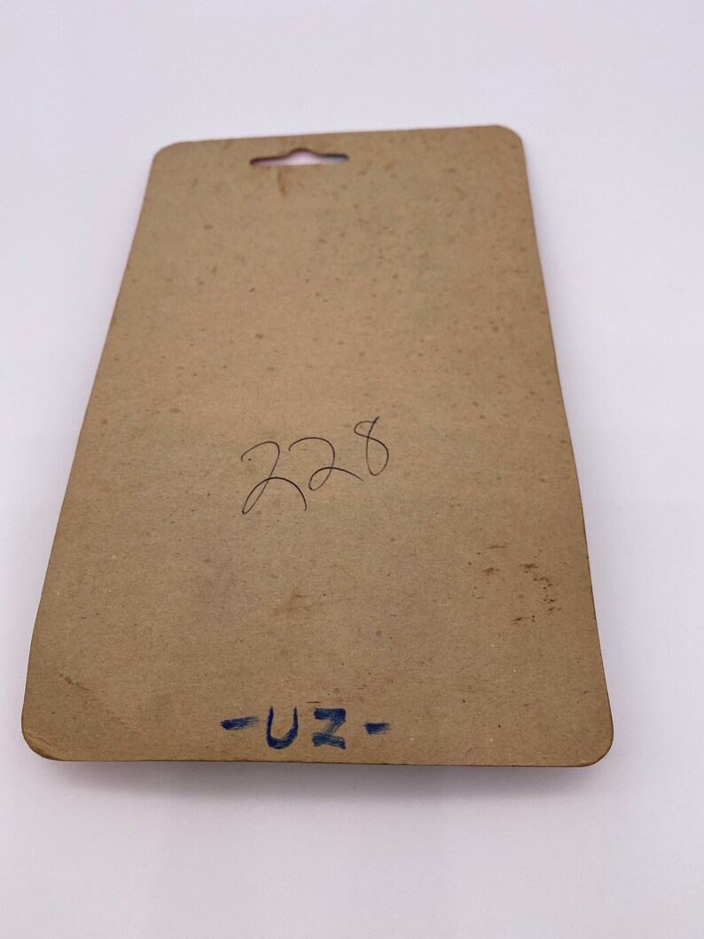 May include: A brown cardboard backing card with a hole at the top for hanging. The card has handwritten text that says "228" and "-UZ-"