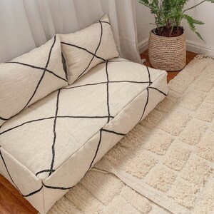 Puede incluir: Un cojín de suelo blanco y negro con estampado con dos almohadas a juego. El cojín está sobre una alfombra blanca de pelo largo.