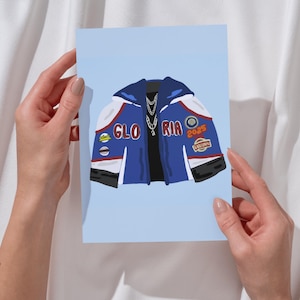 May include: A blue jacket with white and black accents. The jacket has patches that say "Gloria", "Ria", "2025", and "Dolphins". The jacket has a silver chain necklace with a pendant.