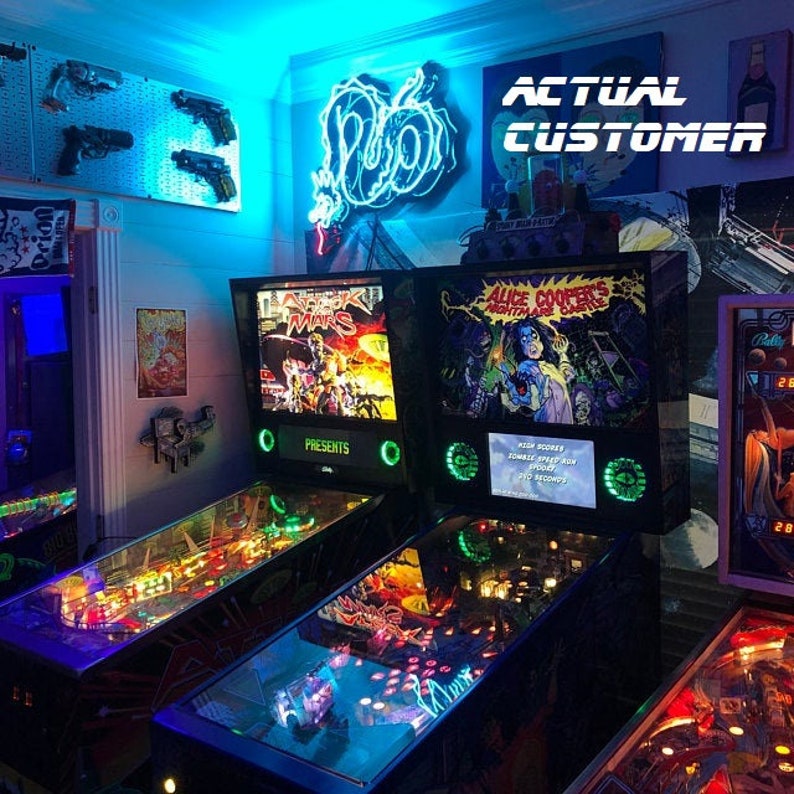 Może przedstawiać: Dwa automaty do gry w pinball z szklanymi powierzchniami do gry. Automat po lewej stronie ma tylny panel ze słowami "Attack Mars" i "Presents". Automat po prawej stronie ma tylny panel ze słowami "Alice Cooper's Nightmare Castle".