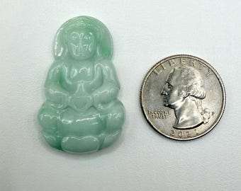 May include: A light green jade Buddha figurine in a seated position, with hands clasped in a meditative pose. The figurine is next to a U.S. quarter for size comparison. The Buddha is carved with details.