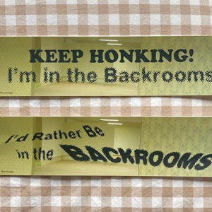 May include: Two rectangular stickers with text. The top sticker reads "KEEP HONKING! I'm in the Backrooms" in black text. The bottom sticker reads "I'd Rather Be in the BACKROOMS" in black text. The background of the stickers is a yellow and beige image.