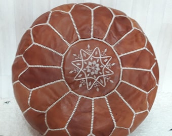 May include: A brown leather pouffe with white stitching and a white embroidered star design.