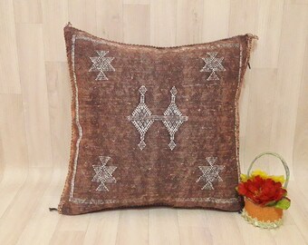 May include: A brown square pillow with a white geometric pattern. The pillow is made of a soft, woven fabric and has a fringed edge.