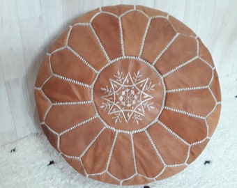 May include: A brown leather pouf with white stitching and a white embroidered star design.