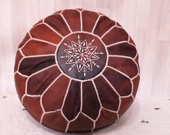 May include: A brown leather pouf with white stitching and a star-shaped design in the center.