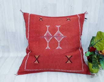 Könnte beinhalten: Rotes quadratisches Kissen mit weißen und orangefarbenen, gestickten geometrischen Mustern. Das Kissen ist aus einem weichen, gewebten Stoff.