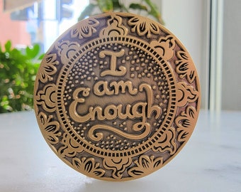 May include: A gold-toned metal token with an ornate design and the words "I am Enough" inscribed in a decorative font.