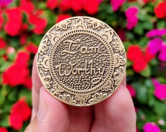 May include: A gold-coloured metal token with an ornate design and the words "I am Worthy" inscribed in the centre.