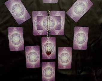 Op de afbeelding: Een tarotkaartlegging met tien kaarten die in een cirkel zijn gerangschikt rond een hanger met een rode hartbedel. De kaarten zijn paars met een wit mandala-ontwerp.