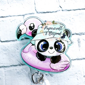 May include: A badge reel featuring a cartoon panda wearing a bucket hat and floating on a pink flamingo pool float. The hat has floral accents and the text "Papercraft & Beyond". The badge reel has a glittery, teal border.