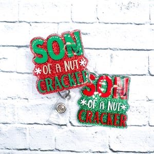 Puede incluir: Dos portagafes de Navidad con purpurina roja y verde con el texto "Son of a Nut Cracker" en cada uno.