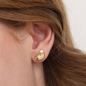Könnte beinhalten: Ohrringe in Goldton mit einem kleinen Teetassen-Design und einem Perlenakzent. Die Ohrringe sind im Stecker-Stil.