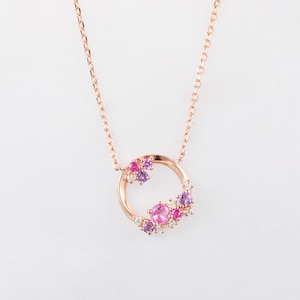 May include: A rose gold necklace featuring a delicate chain and a circular pendant. The pendant is partially adorned with a cluster of small, round-cut pink and purple gemstones, accented by tiny clear stones along the metal frame.