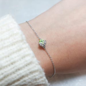 May include: A delicate silver chain bracelet with a green gemstone and diamond accents in the shape of a leaf.
