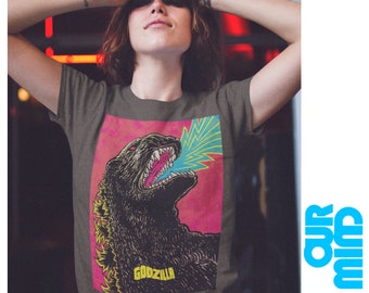 May include: Dark gray t-shirt featuring a Godzilla graphic. The graphic shows Godzilla roaring with a blue and yellow energy blast against a pink background. The word "GODZILLA" is printed in yellow at the bottom of the graphic.